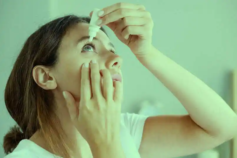 Technician handling ophthalmic dropper bottles under cleanroom lighting.